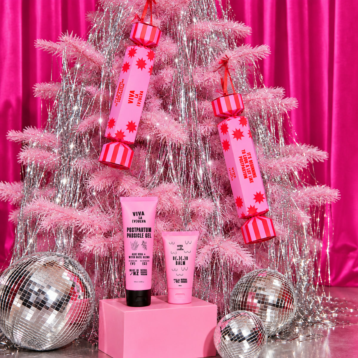 Two Viva La Vulva Christmas crackers hanging on a pink tinsel tree with Padsicle Gel and B( . )( . )B Balm below